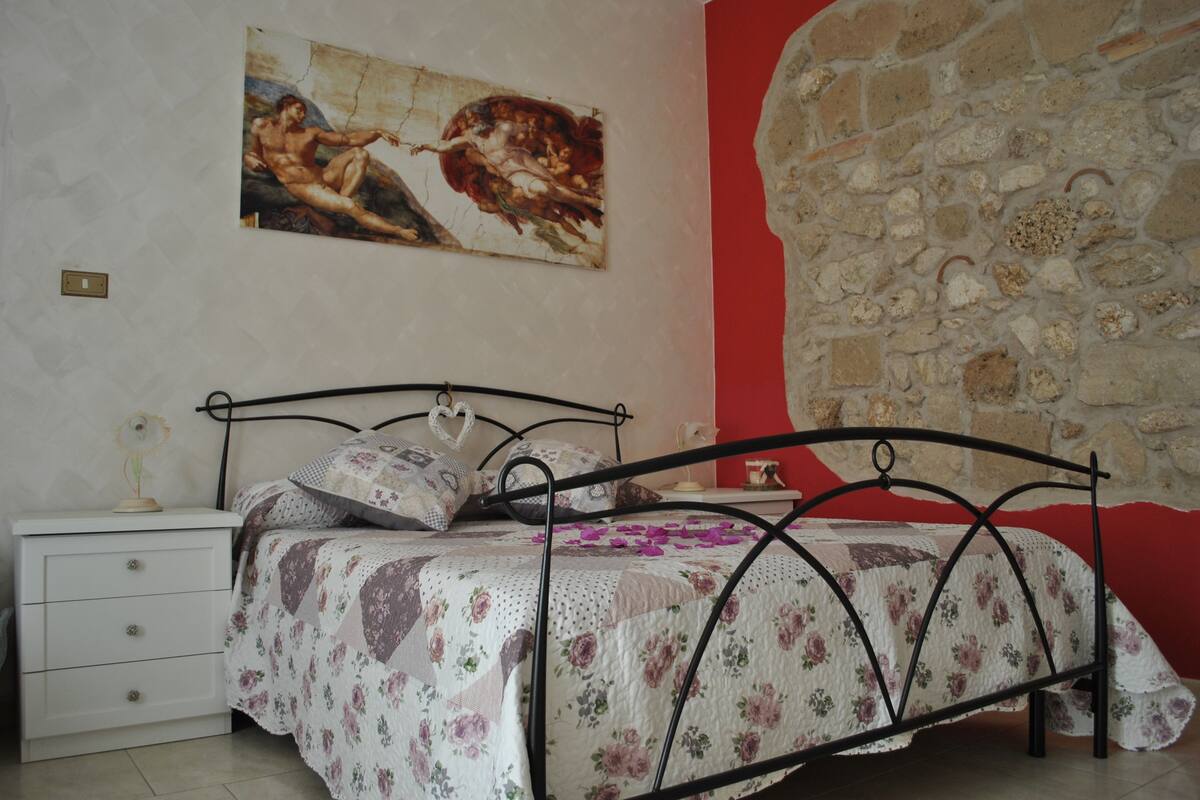 Un dormitorio con una cama, una mesita de noche, un cuadro y una pared de piedra.
