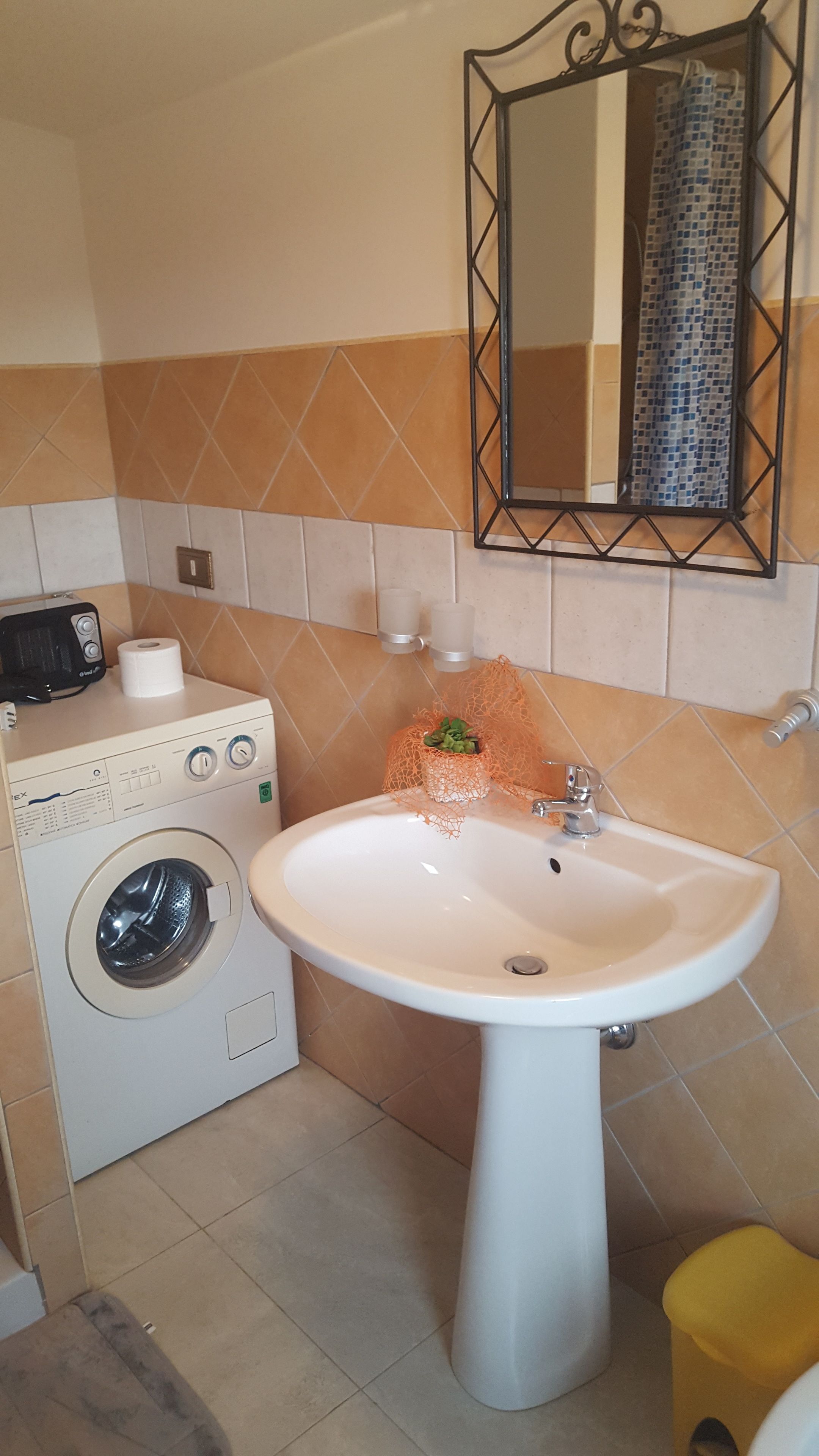 A compact bathroom with a washing machine, sink, and a mirror above the sink.
