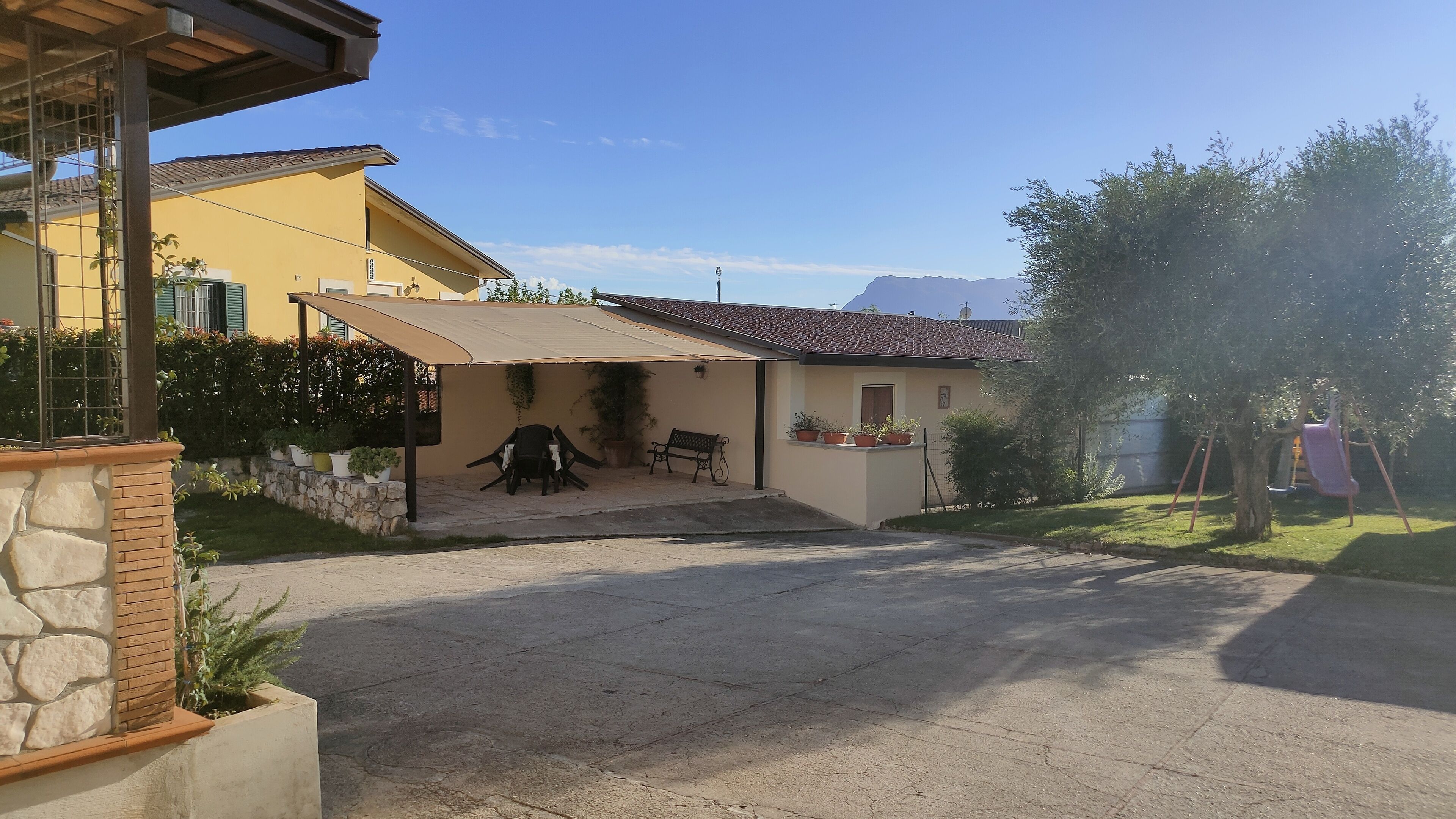 A residential property with a paved driveway, a covered patio area, and a small garden with potted plants.