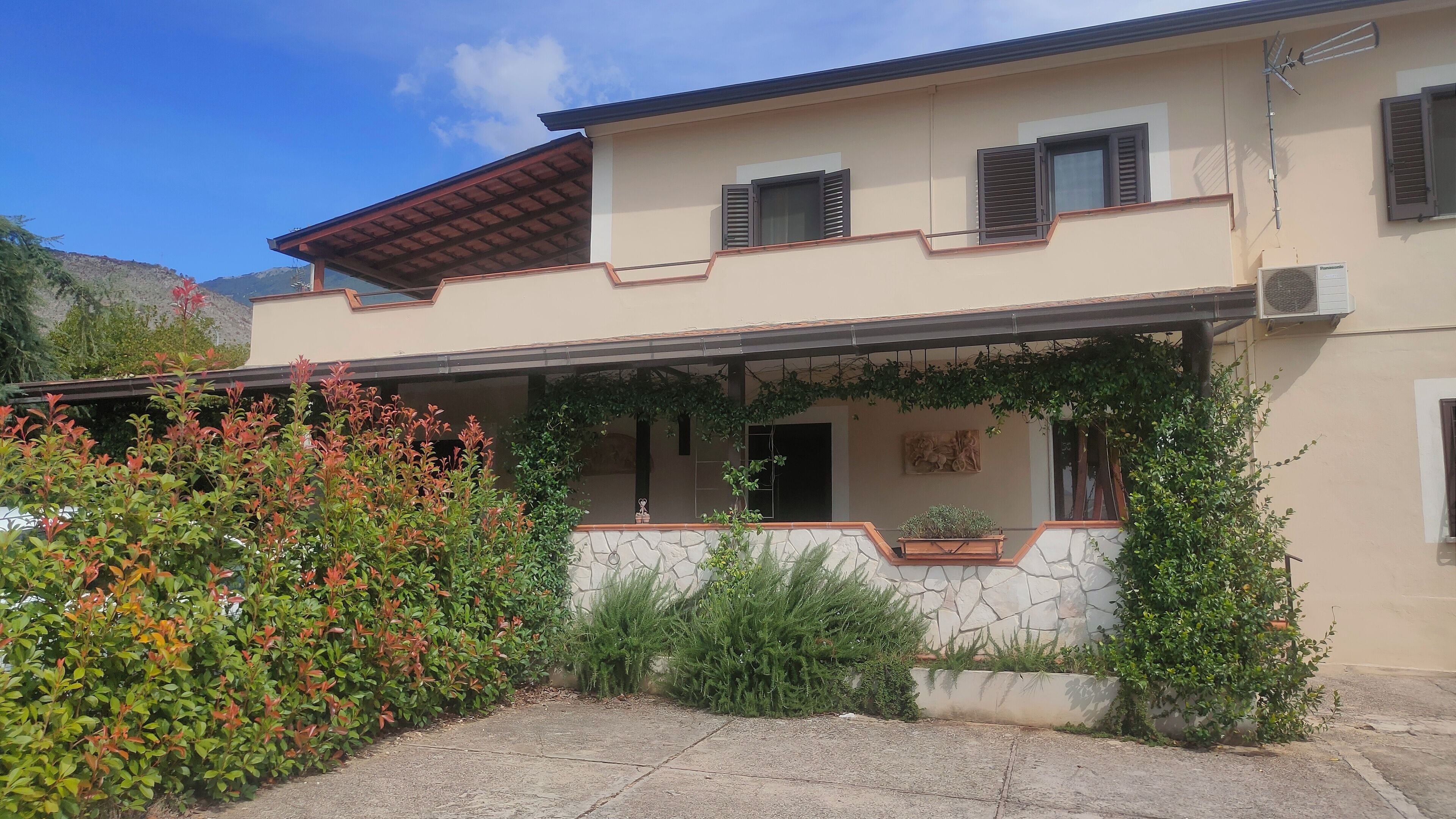 A two-story house with a stone facade, a covered porch with greenery, and a mountain backdrop.