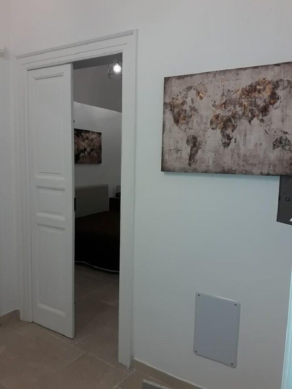 A hallway with a white door, a world map artwork on the wall, and a vent.