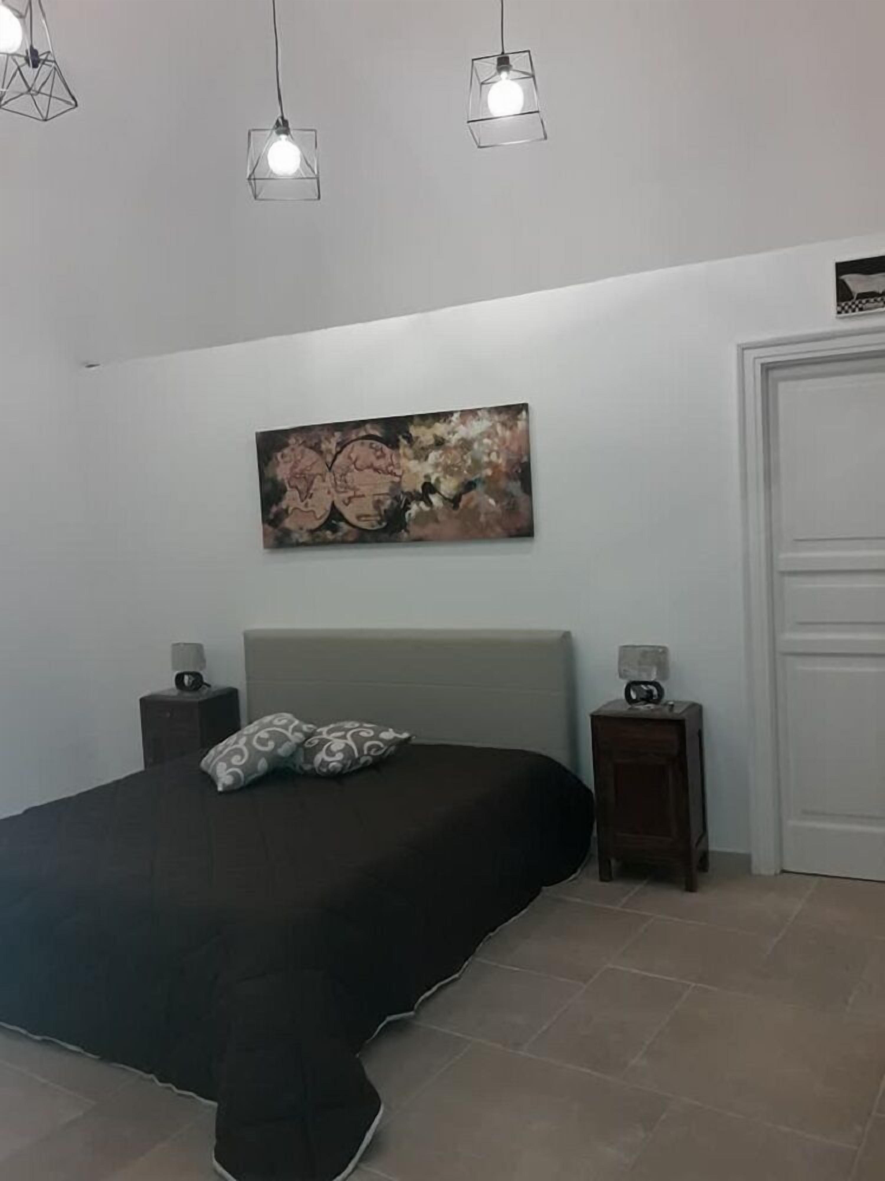 Un dormitorio con cama, mesita de noche, cuadro en la pared y una puerta.