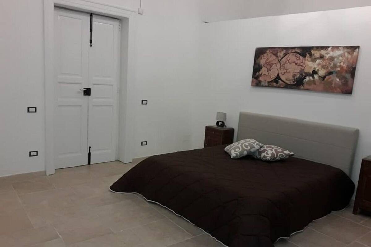 A bedroom with a bed, a nightstand, a wall-mounted painting, and a door.