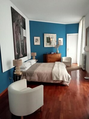Une chambre à coucher avec un lit, une commode, une chaise et des œuvres d’art accrochées aux murs.