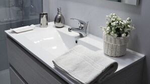 A modern bathroom with a white vanity, a glass shower enclosure, a large mirror, and a small potted plant. - Altera Domus (Naples)