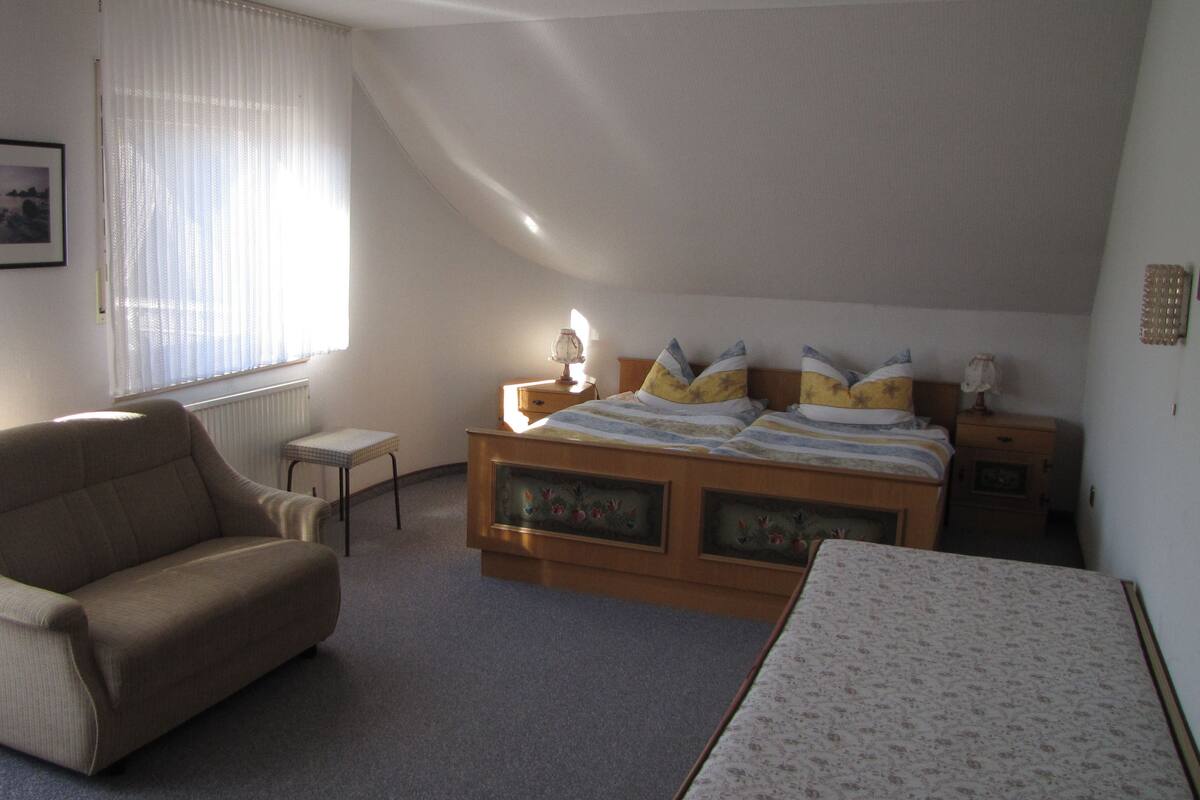 A bedroom with a single bed, a chair, a small table, and a radiator.