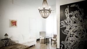 A modern living room with a white sofa, a round coffee table, and a chandelier. There is a large black and white artwork on the wall. - Angelina B&B Dimora Contemporanea (Rome)