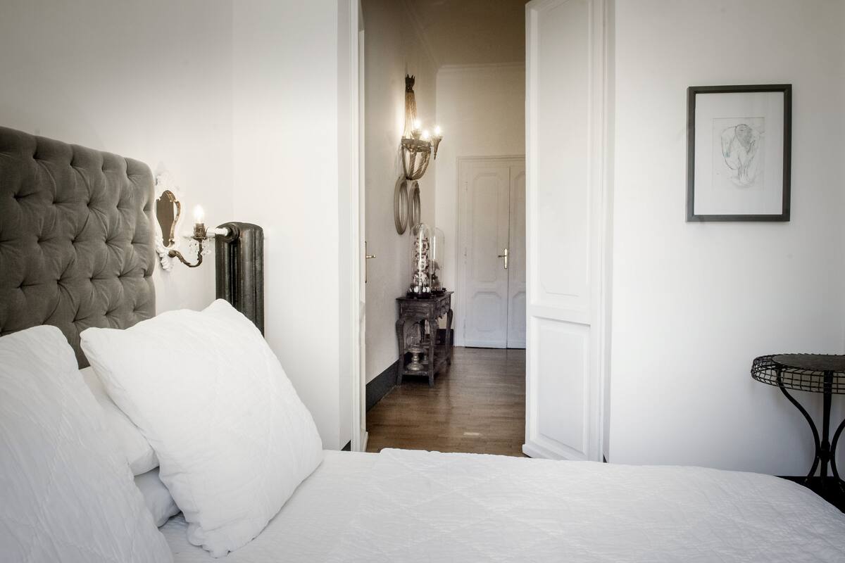 A bedroom with a tufted headboard, a bedside table, a lamp, and a framed artwork on the wall.