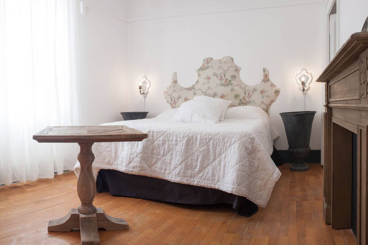 A bedroom with a wooden bed, white bedding, two bedside tables with lamps, and a wooden floor.
