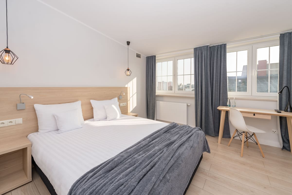 Une chambre d’hôtel moderne, dotée d’un grand lit, d’un bureau et offrant une vue sur la ville.