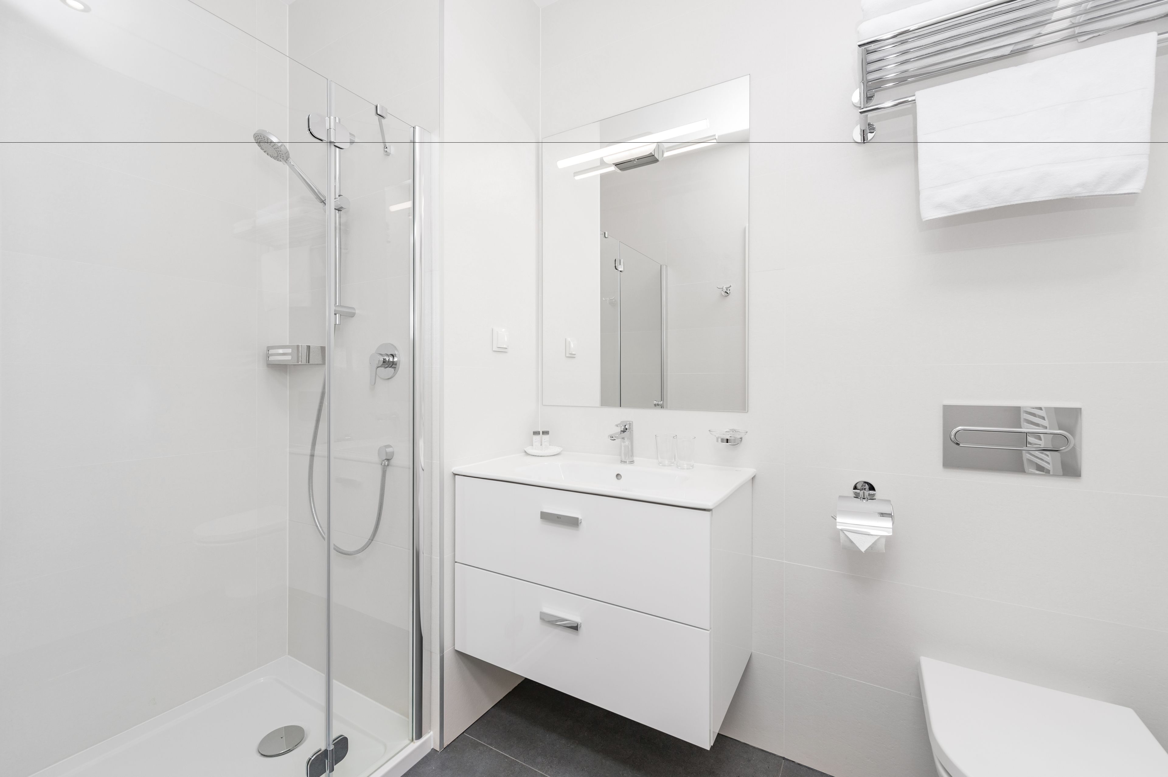 Un baño moderno con cabina de ducha de vidrio, tocador blanco con espejo y un inodoro.