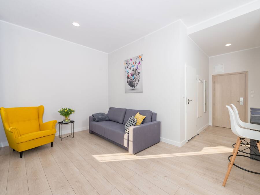 Una sala moderna con un sillón amarillo, un sofá gris y una silla de comedor blanca.
