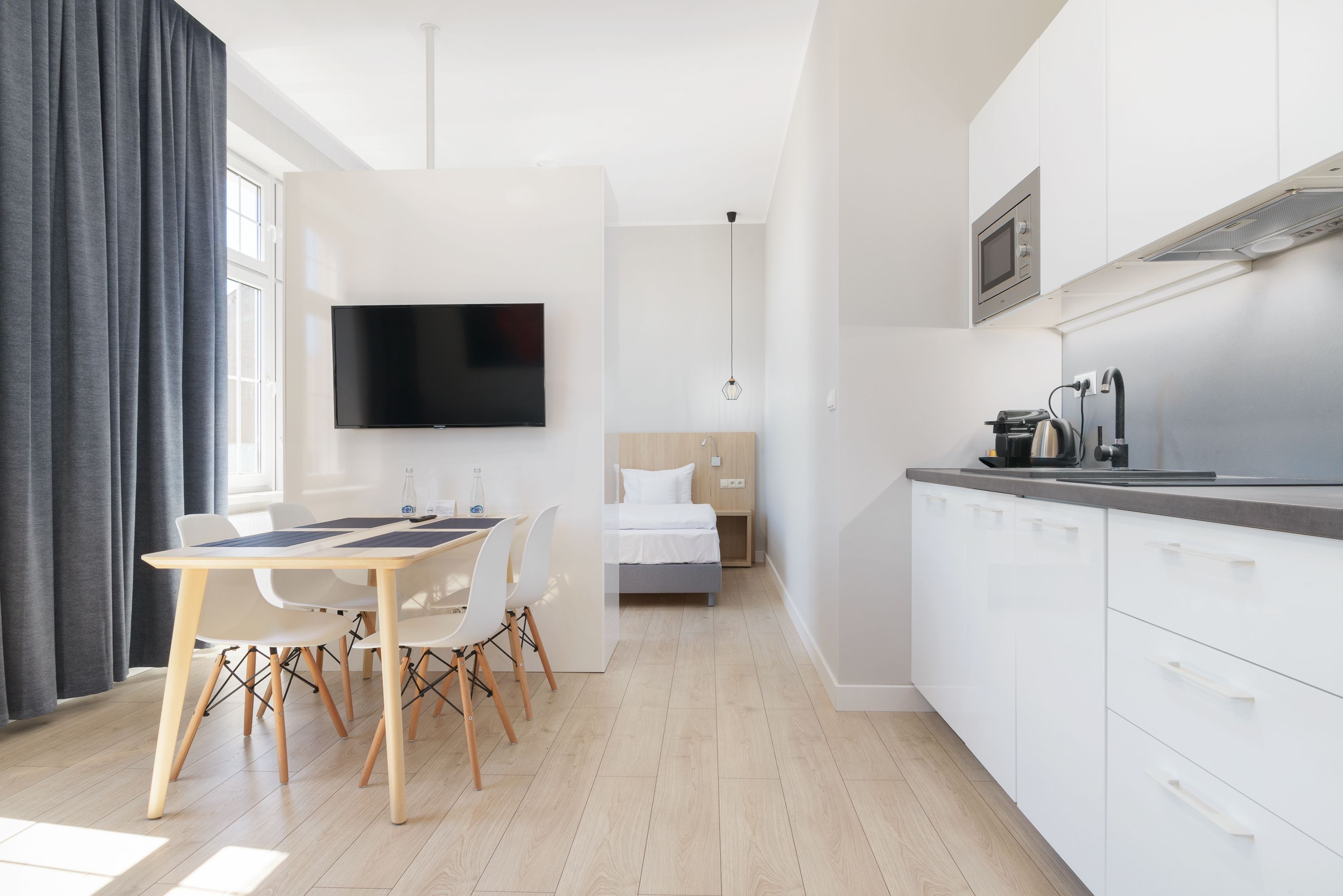 A modern, well-lit room with a dining area, a bed, and a kitchenette.