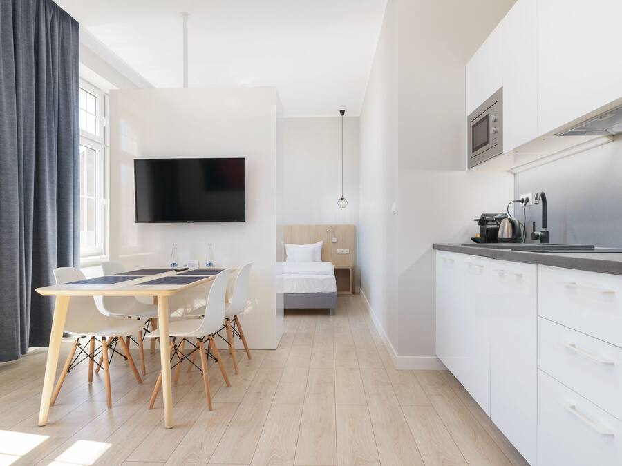 A modern, well-lit room with a dining area, a bed, and a kitchenette.