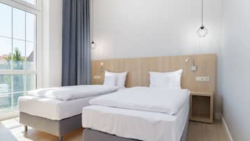 Ein modernes Schlafzimmer mit zwei Einzelbetten, einem Holzkopfende, Nachttischlampen und einem großen Fenster mit Vorhängen.