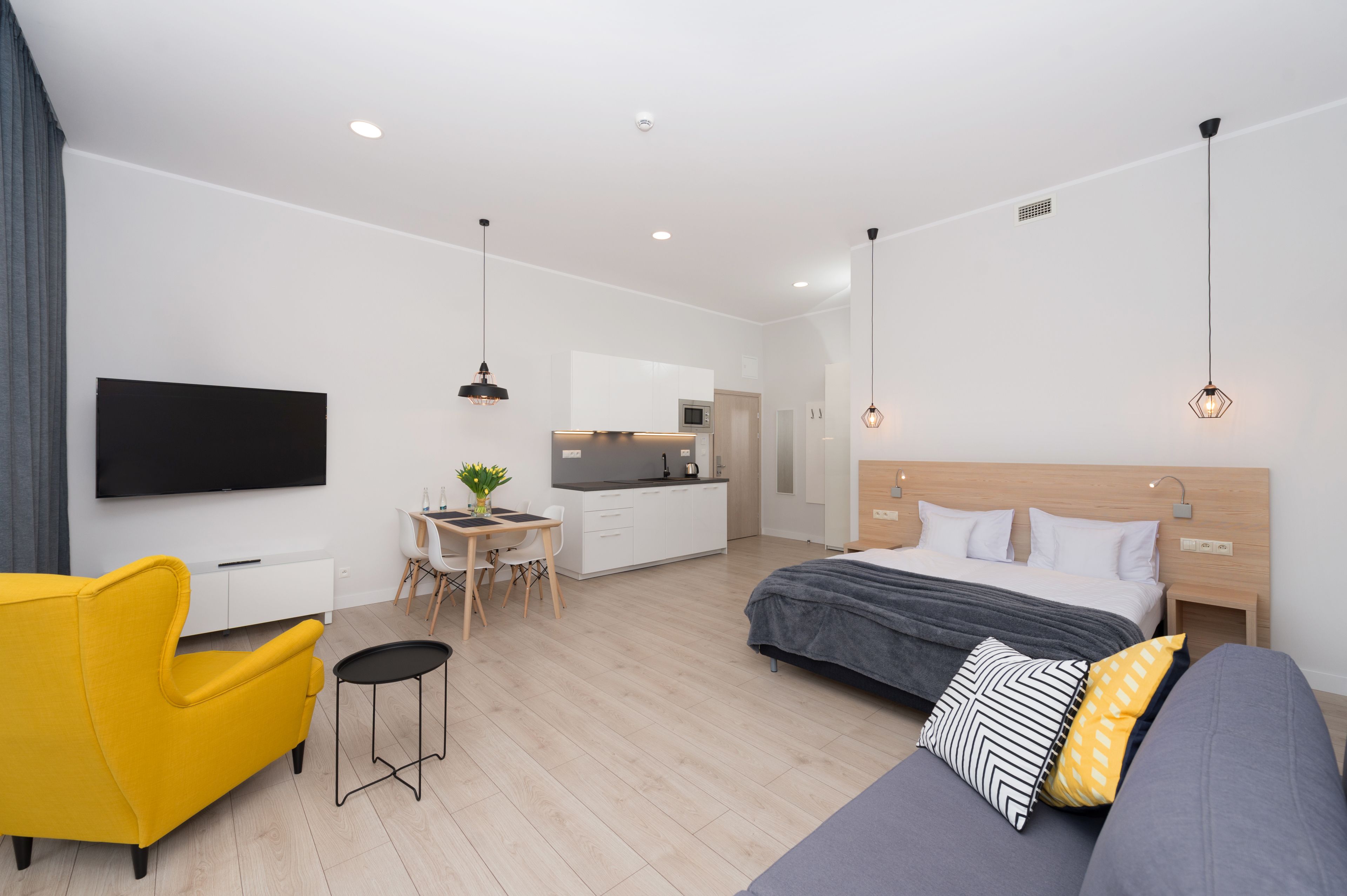 A modern hotel room with a bed, a sofa, a desk, and a TV.