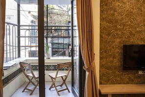 A room with a large window, two wooden chairs, a potted plant, and a flat-screen TV on a marble wall. - Carrot Haus (Hanoi)