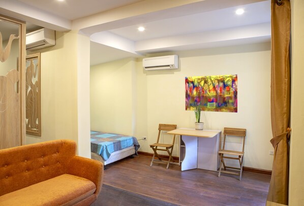 A room with a bed, an orange sofa, a small table, two chairs, and a colorful painting on the wall.