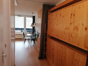 A room with a wooden wardrobe, a dining table with chairs, and a window with a view. - Southwest studio in Val-Claret, near shops (Tignes)