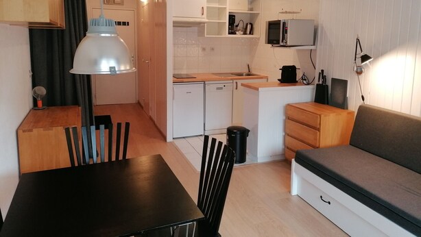 Kompakti keittiö, jossa on astianpesukone, mikroaaltouuni sekä pieni ruokailutila, jossa on pöytä ja tuolit.