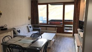 A compact living space with a sofa, a dining table with chairs, a small kitchen area, and large windows offering a view of the city. - Studio in Tignes with wifi near the slopes (Tignes)