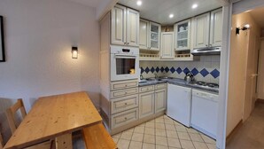 A compact kitchen with white cabinets, a built-in oven, a sink, and a wooden dining table. - Southwest studio in Tignes, near slopes, 27 m² (Tignes)