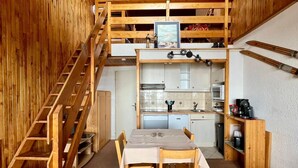 A compact, multi-level room with a wooden staircase, a kitchenette, a dining area, and ski equipment on the wall. - 2-room south-facing, ski-in/ski-out, balcony, TV, linen included (Tignes)
