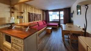 A compact living space with a kitchenette, a sofa, a dining table, and a view of a building through a window.