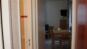 Ein Zimmer mit einem Holzespeisetisch und Stühlen, einem Fernseher an der Wand und einer Tür mit rotem Streifen.