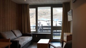 Une pièce avec un mur recouvert de panneaux de bois, un canapé gris, une table en bois et une chaise.