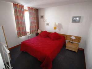 Une chambre à coucher avec un grand lit, une tête de lit en bois, une table de chevet, une lampe et une fenêtre avec des rideaux.