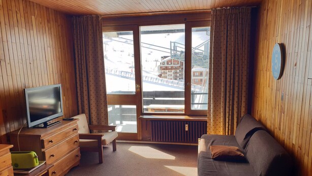 A cozy room with a wooden interior, a sofa, a television, a dresser, and a window with a view of buildings and a bridge. - Studio at the foot of the slopes with south balcony in Tignes (Tignes)