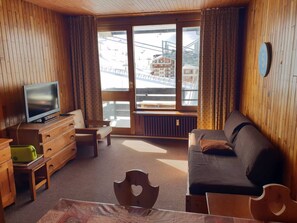 A cozy room with a wooden interior, a sofa, a television, a dresser, and a window with a view of buildings and a bridge.
