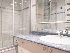 Ein modernes Badezimmer mit Duschkabine aus Glas, einem weißen Waschbecken und einer Granit-Arbeitsplatte sowie einem großen Spiegel darüber.