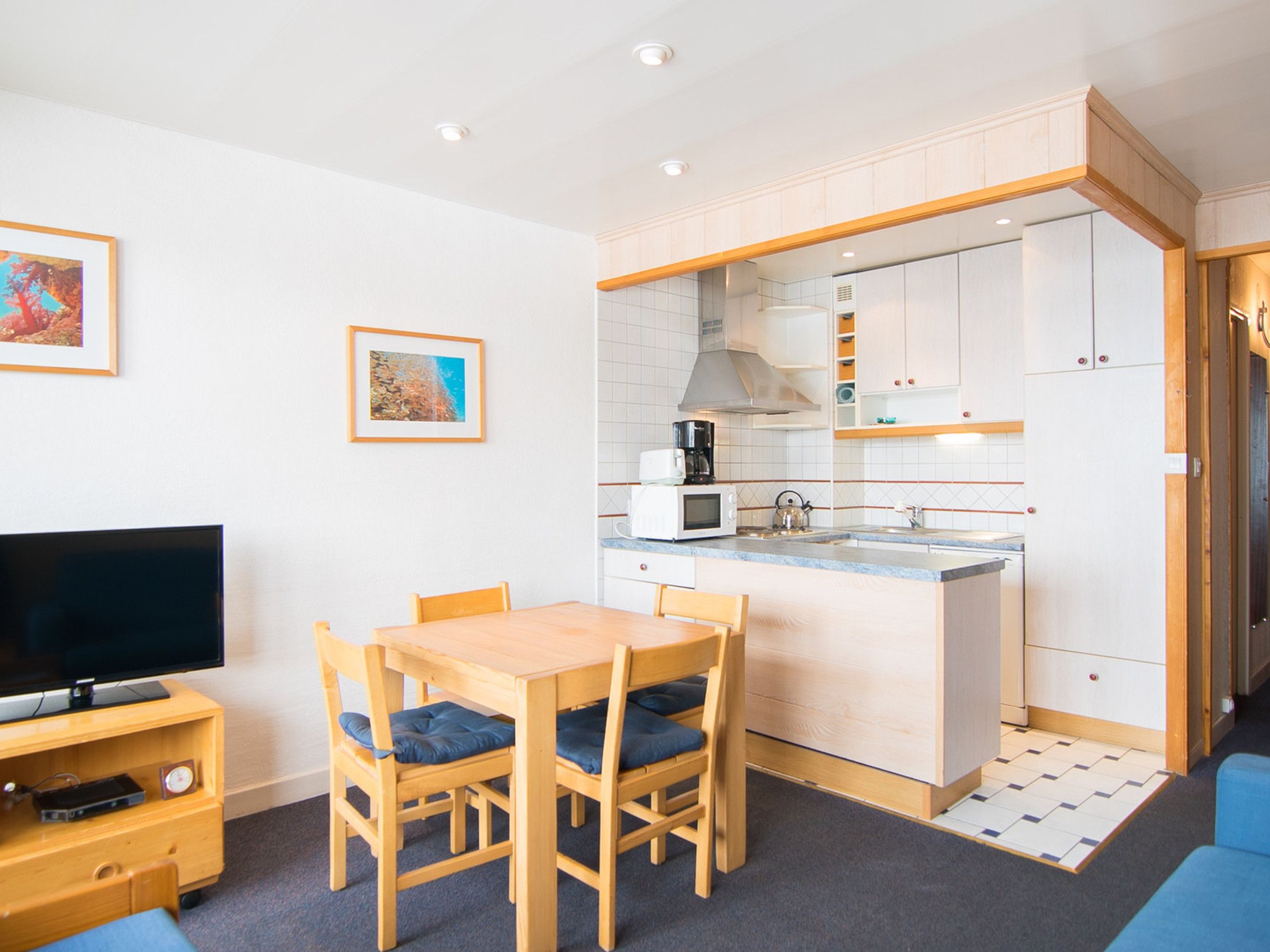 A compact kitchen with a microwave, kettle, and coffee maker. There is a dining table with chairs and a flat-screen TV on a wooden stand.
