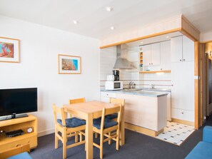 A compact kitchen with a microwave, kettle, and coffee maker. There is a dining table with chairs and a flat-screen TV on a wooden stand.