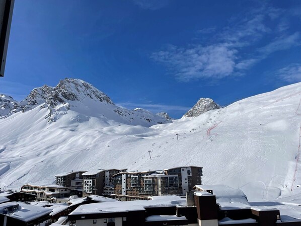 A snow-covered mountain with a ski resort in the foreground, featuring multi-story buildings with balconies and ski lifts visible.
