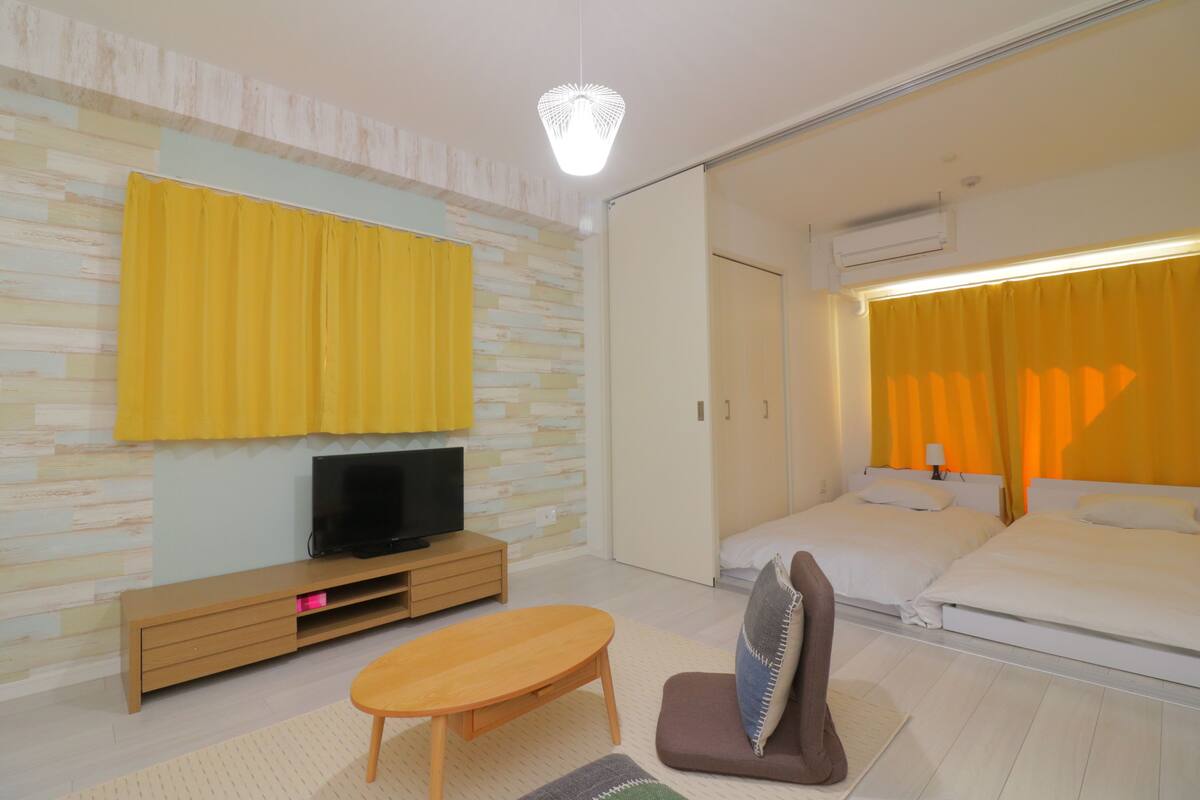 A modern hotel room with a flat-screen TV on a wooden TV stand, a sofa, a small table, and a bed with white bedding.