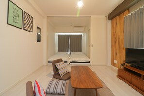 A compact living space with a sofa, a small table, a television, and a window with curtains. - Modern Apartment Osaka Dome Mae (Osaka)