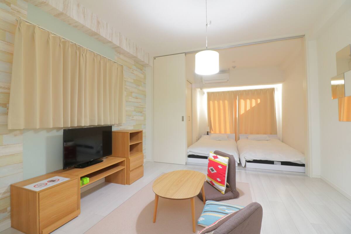 A compact hotel room with a flat-screen TV, a sofa, a small table, and a bed.