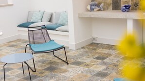 Une pièce avec un sol à motifs, une chaise bleue, une petite table, un canapé avec des coussins à motifs et des objets décoratifs sur une étagère.