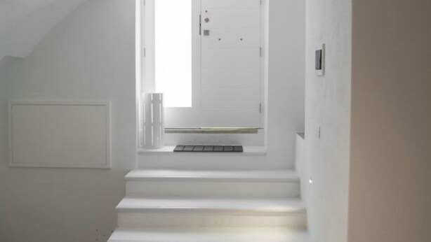 Un escalier menant à une porte dans une pièce minimaliste aux murs blancs et à la petite fenêtre.