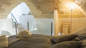 Une pièce chaleureuse avec un plafond en pierre, un lit recouvert d’une couette beige et une table de chevet avec une lampe.
