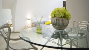 Une table ronde en verre, ornée d’un vase de fleurs vertes, d’un flacon de parfum et d’une petite plante posée sur une chaise blanche.