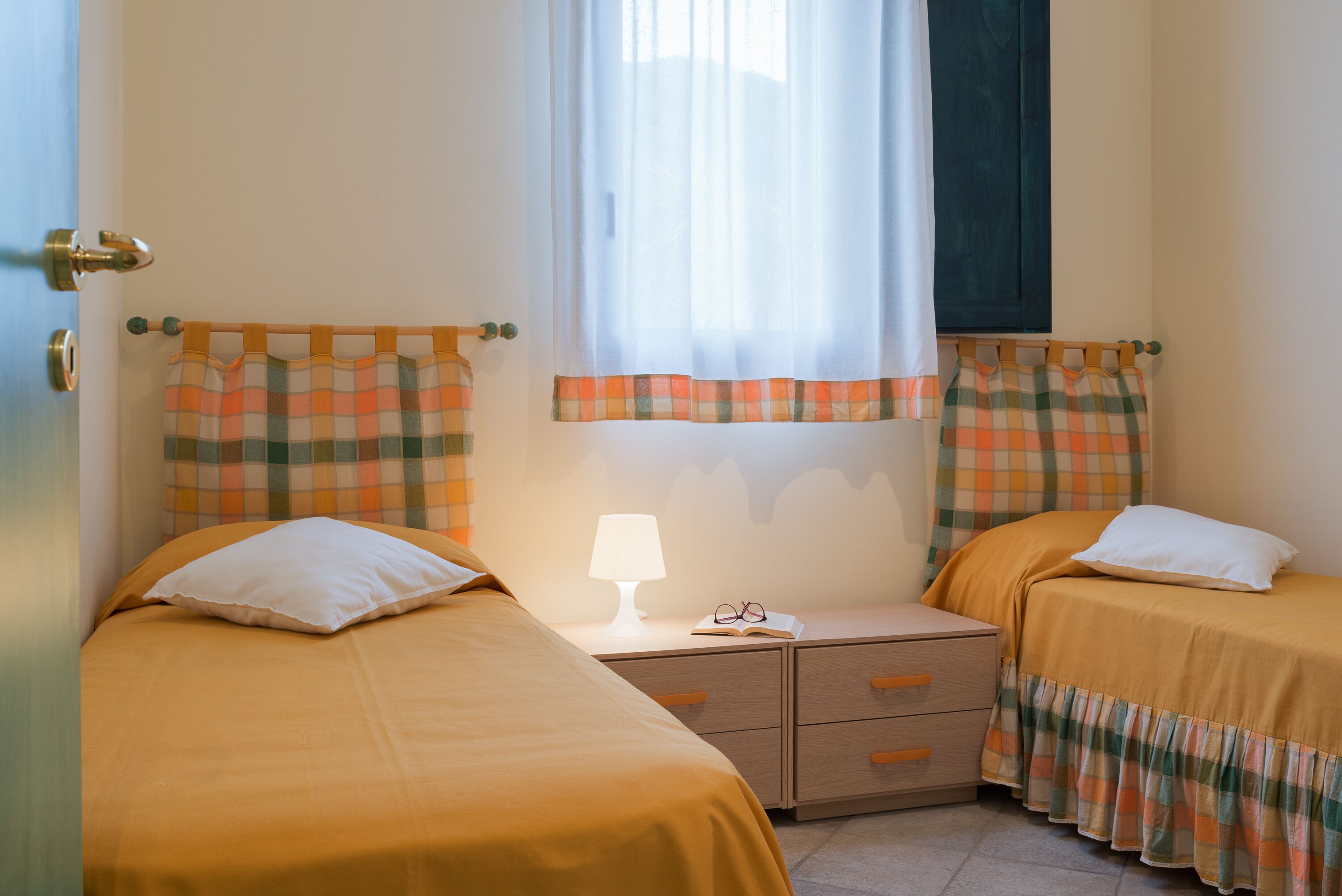A bedroom with two beds, a nightstand, a lamp, and a window with curtains.