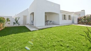 Een modern wit huis met een plat dak, een kleine voortuin en een eethoek met tuinmeubilair.