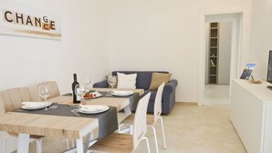 Een moderne eetruimte met een houten tafel gedekt voor vier personen, witte stoelen en een grijze bank op de achtergrond.
