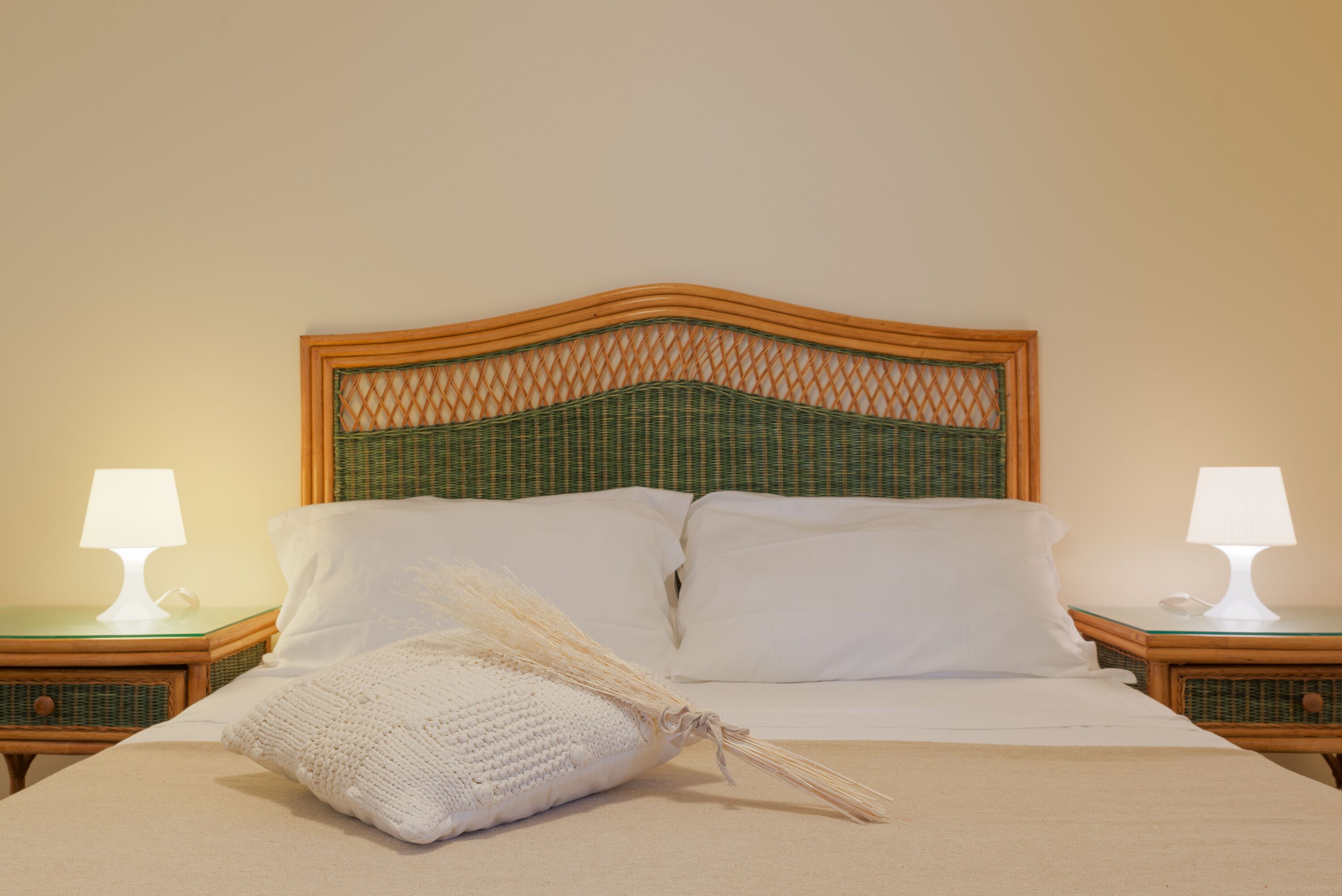 A neatly made bed with white linens, a woven headboard, and two bedside lamps on wooden nightstands.