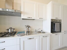 Una cocina moderna con armarios blancos, estufa de acero inoxidable, horno empotrado y pileta.