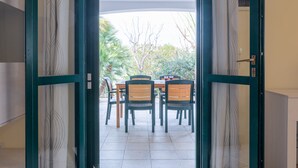 Een open deur die leidt naar een terras met een tafel en stoelen, omgeven door een groene omlijsting en behang met patroon.